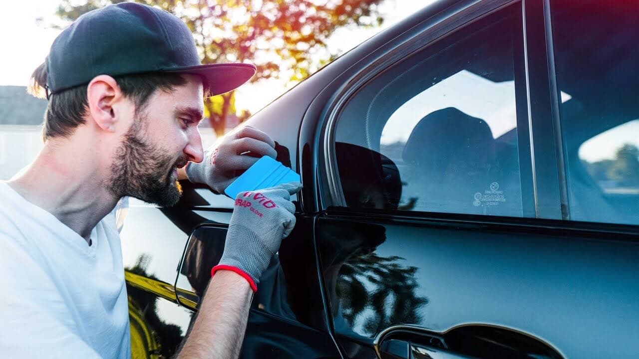 Man in cap applying chrome delete wrap to a car window