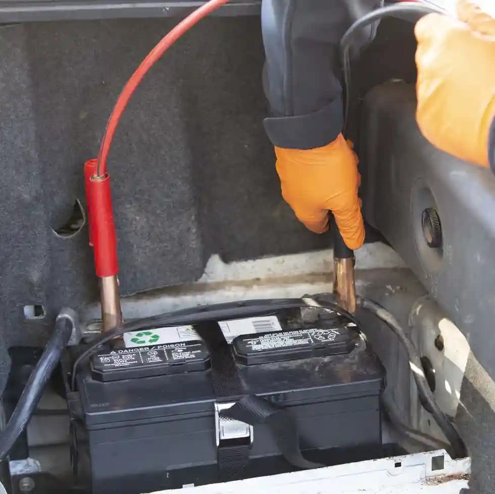 Technician attaching jumper cables to car battery for jump-start service